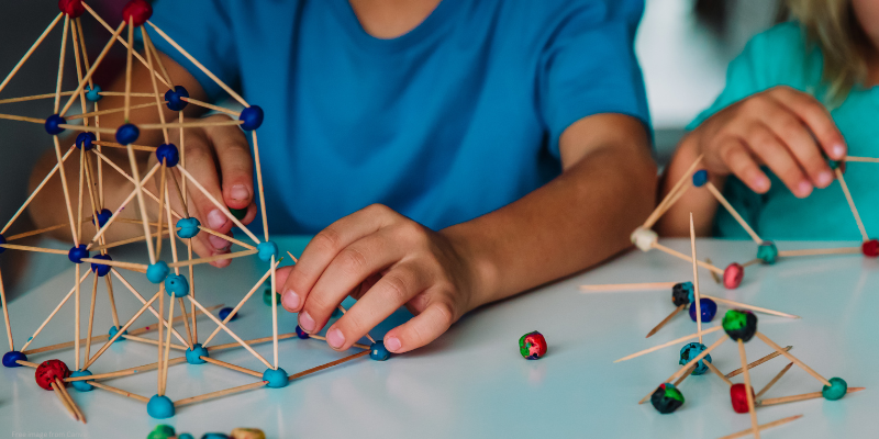 children building structures with sticks and colorful connectors at a table