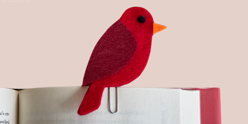 A red felt bird-shaped paper clip on an open book.