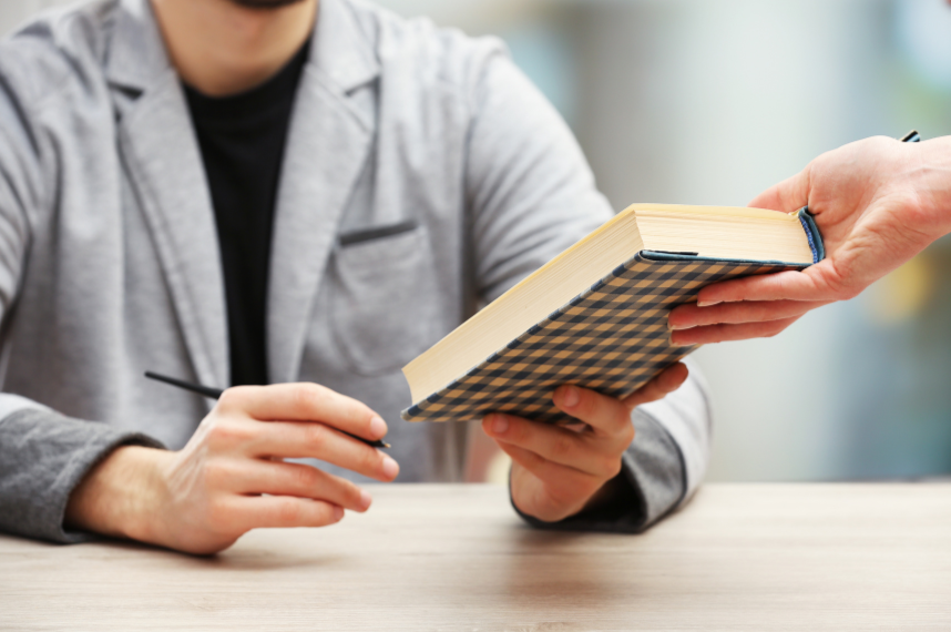 a person handing a book to another person (author) to sign