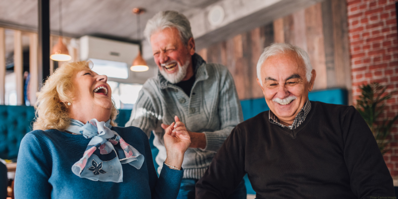 Three elderly individuals laughing together indoors.