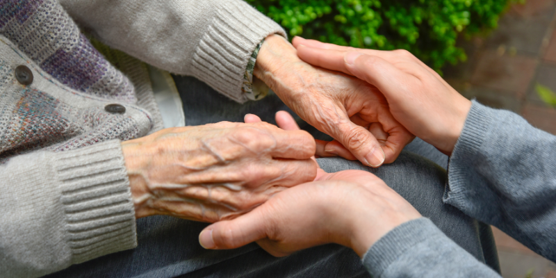 zoom in of adult holding hands with an elderly person
