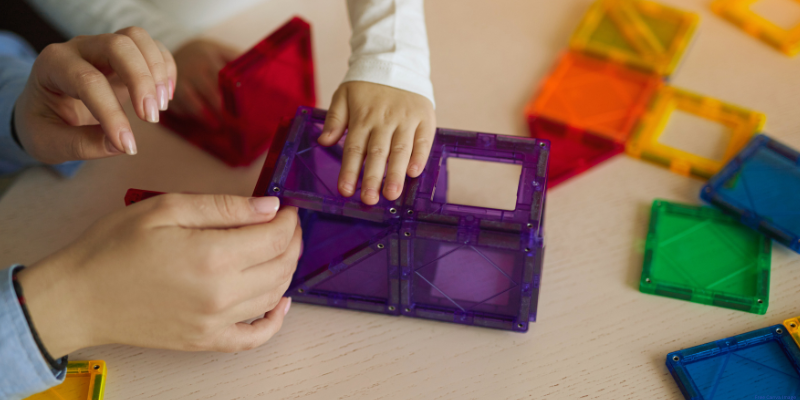 adult and child hands putting together colorful magnetic tiles