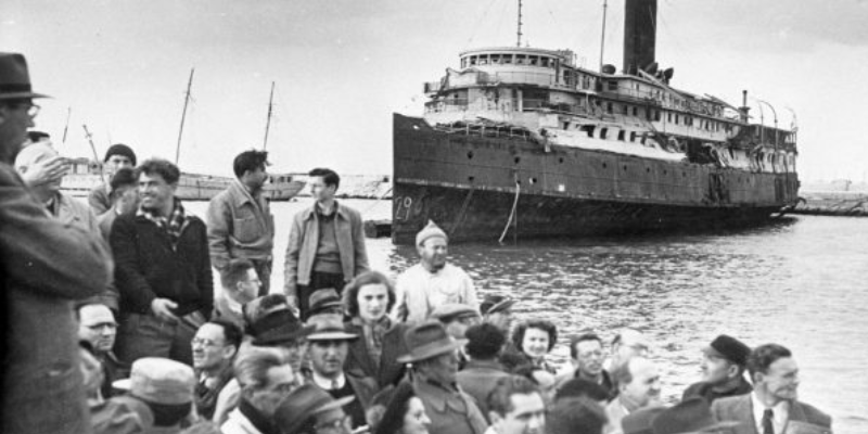 A vintage picture of a crowd of people near a large docked passenger ship.