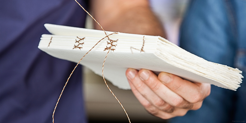 Close-up of a hand holding a handmade book with cross-stitch binding.