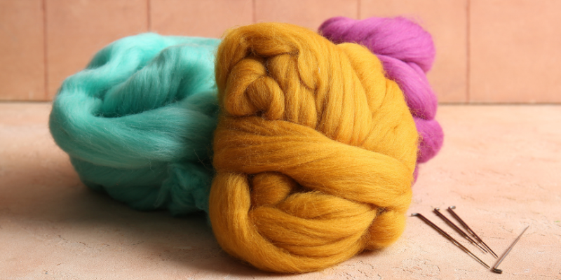 three balls of colored wool and felting needles