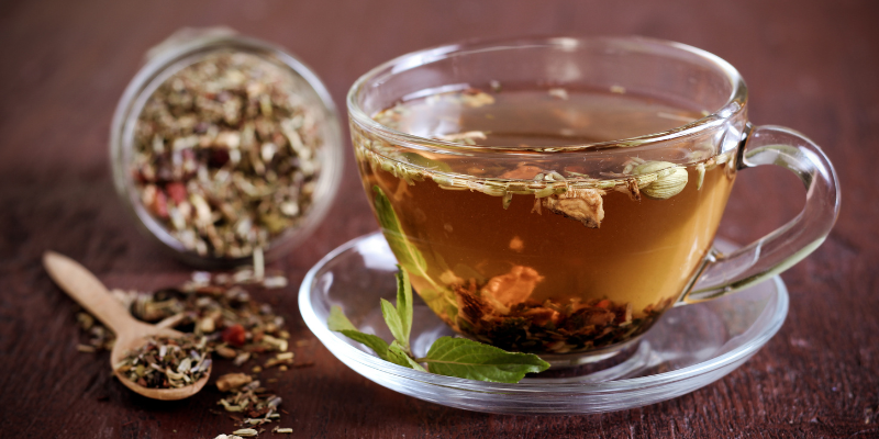 cup of tea with a blend of flowers, spices, and herbs nearby