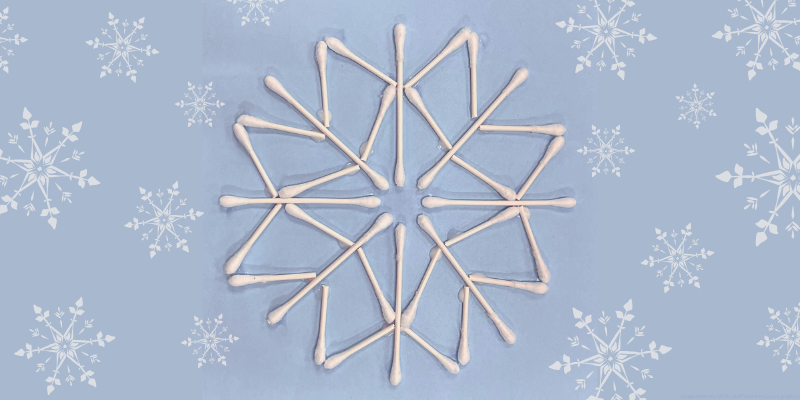 large snowflake outline arranged with cotton swabs and glued to construction paper with snowflake graphics around it