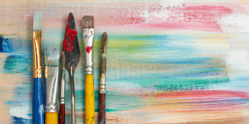 Paintbrushes and a palette knife against a colorful painted background
