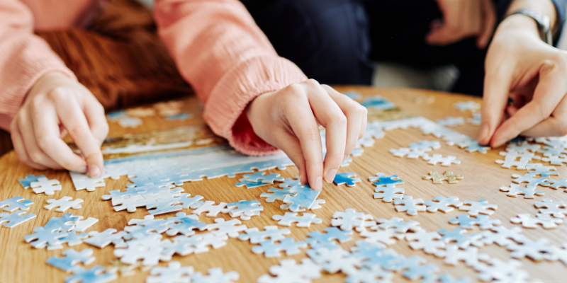 Two people working on a jigsaw puzzle on a wooden table