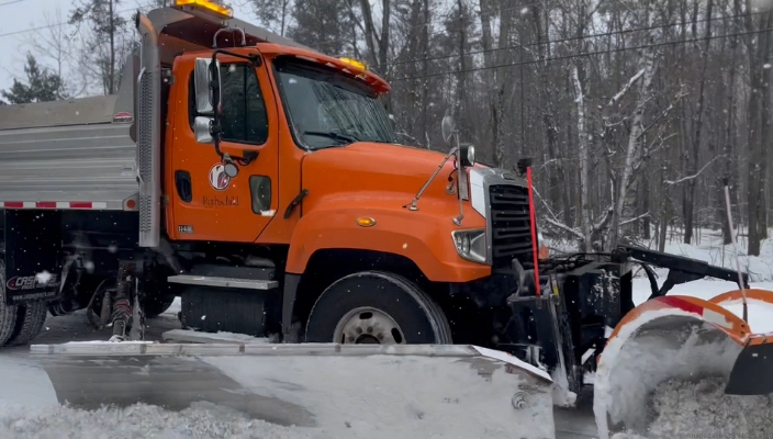 An orange snowplow truck clearing snow on a snowy street.