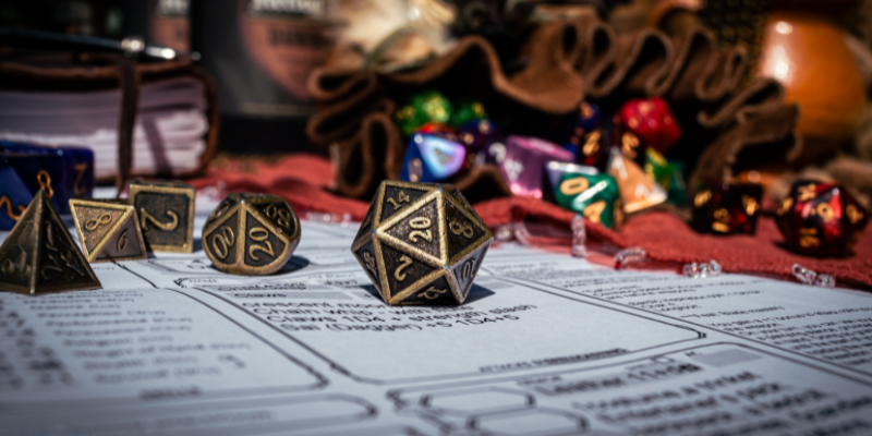 Close-up of a d20 dice on a tabletop roleplaying character sheet with other gaming dice and books in the background.