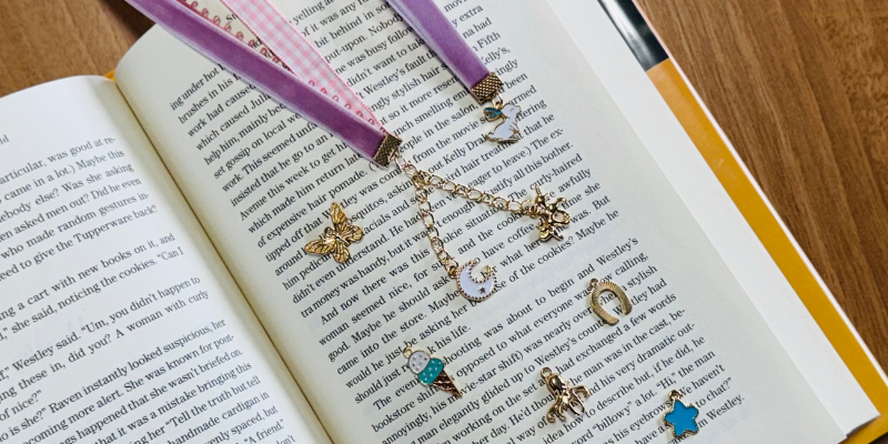 An open book with various gold and colorful charms laid on the pages, attached to purple ribbons