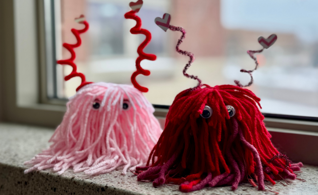 Two yarn creatures with googly eyes and heart-topped pipe cleaners on a windowsill.