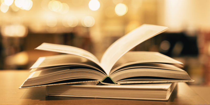 An open book on top of a closed book with warm lighting and blurred background.