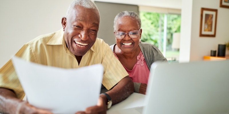Elderly couple smiling at a laptop screen in a bright room.