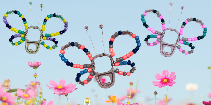 Three beaded butterflies made with soda can tabs over a field of pink cosmos flowers and a blue sky.