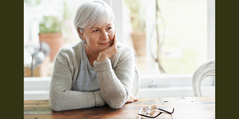Elderly person sitting at a table, resting their chin on their hand looking in the distance