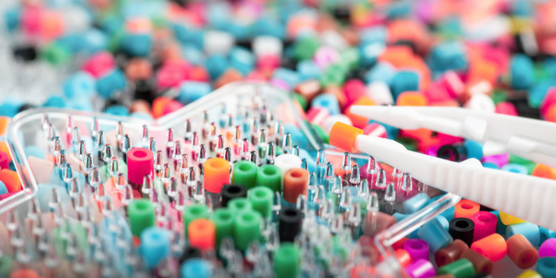 Close-up of colorful beads and a star-shaped sorting tray with tweezers holding an orange bead.