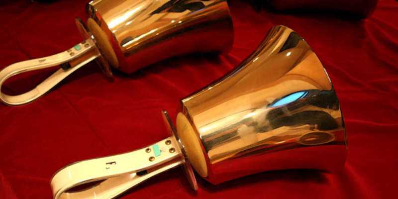 Two brass handbells with white handles rest on a red cloth.