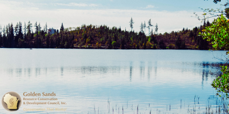 small calm lake with a forest and small house on the far shore