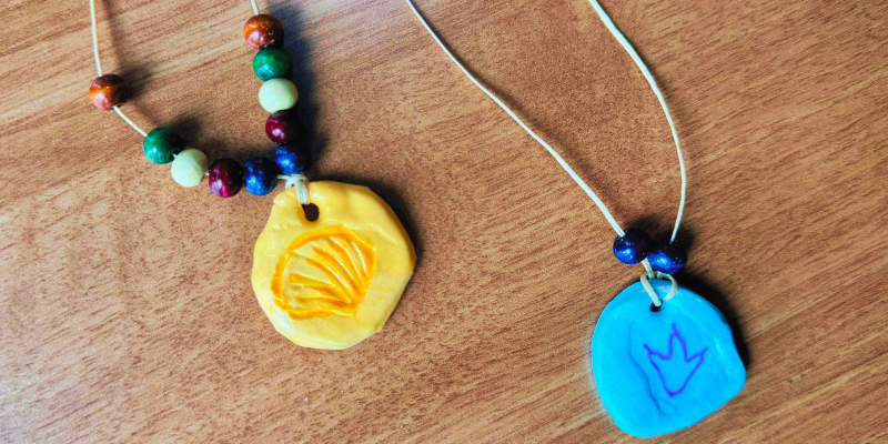 two hand-crafted clay pendants, one yellow with a shell design and one blue with a dinosaur footprint design.