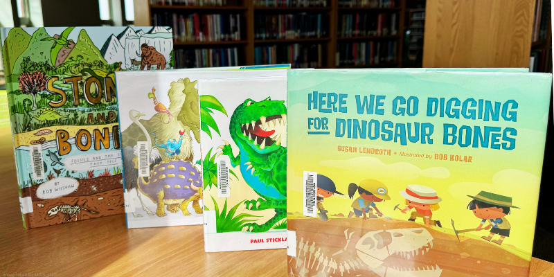 Children's books with dinosaur themes displayed on a library table.