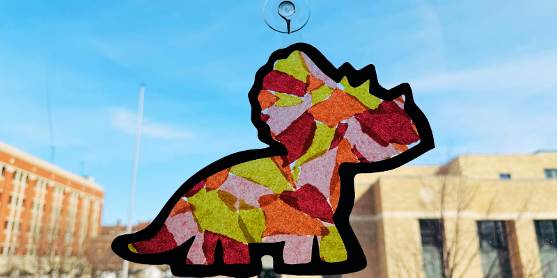 triceratops suncatcher made of contact paper and tissue paper hanging on a window
