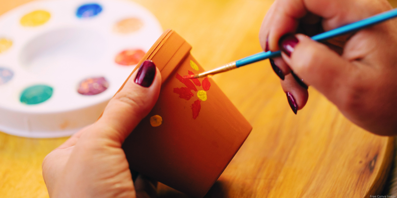 close up of hands painting a flower design on a small terracotta pot