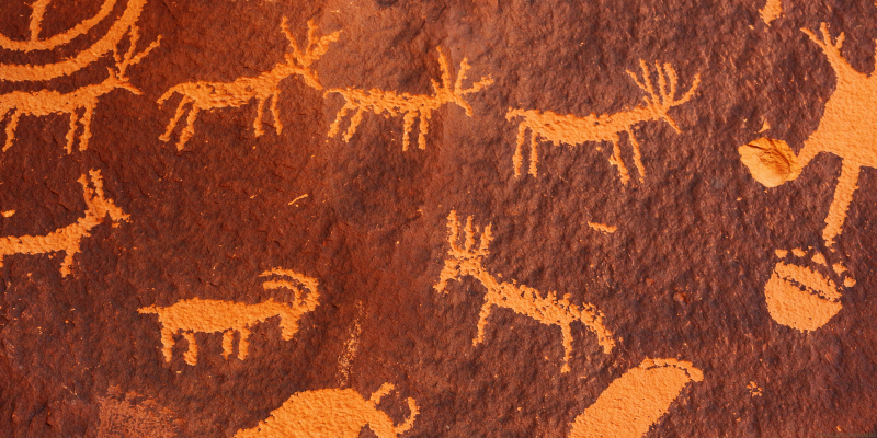 Petroglyphs of animals and circular patterns on a reddish-brown rock surface.