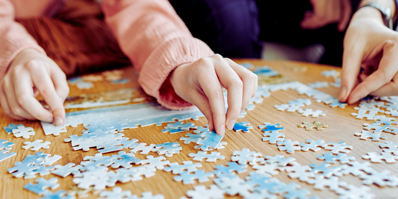 close up of two people working on a puzzle at a table