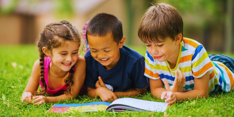 children reading a book in the grass