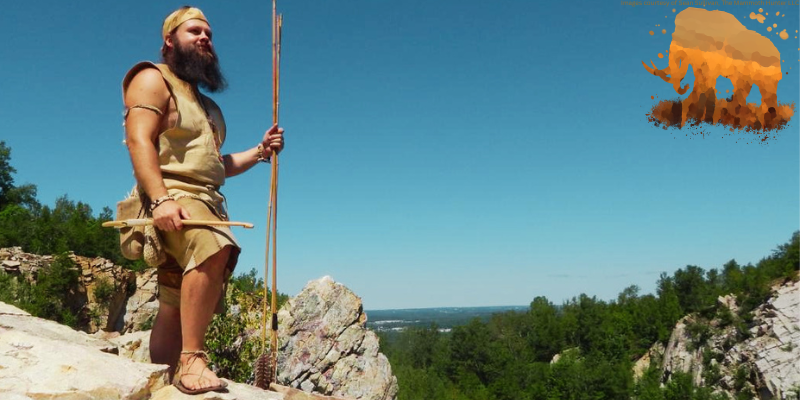 sean, the mammoth hunter, standing on a cliff dressed in prehistoric clothing with a mammoth logo in the upper right corner