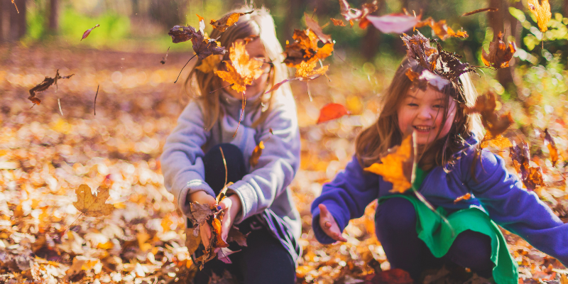 two children playing in fall leaves and throwing them in the air